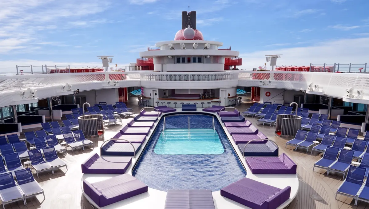 Pool deck with purple loungers on a Virgin Voyages ship under a blue sky